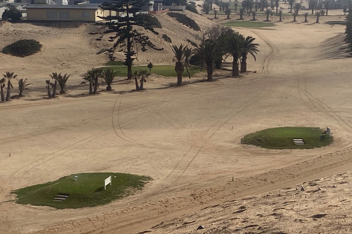 An elevated view of a sandy residential plot featuring landscaped green mounds and mature palm trees within a coastal desert environment.