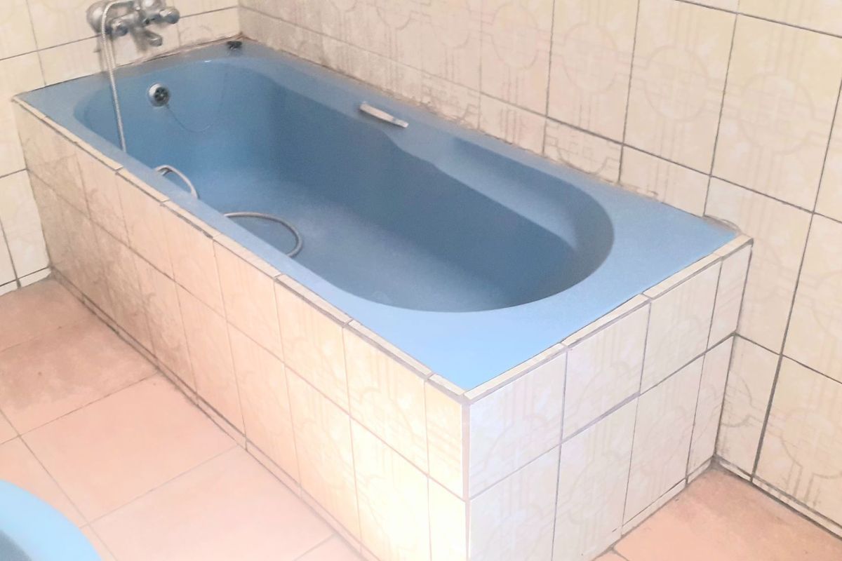 A dated bathroom featuring a built-in blue bathtub with tiled surround and wall finishes, offering potential for a modern renovation.