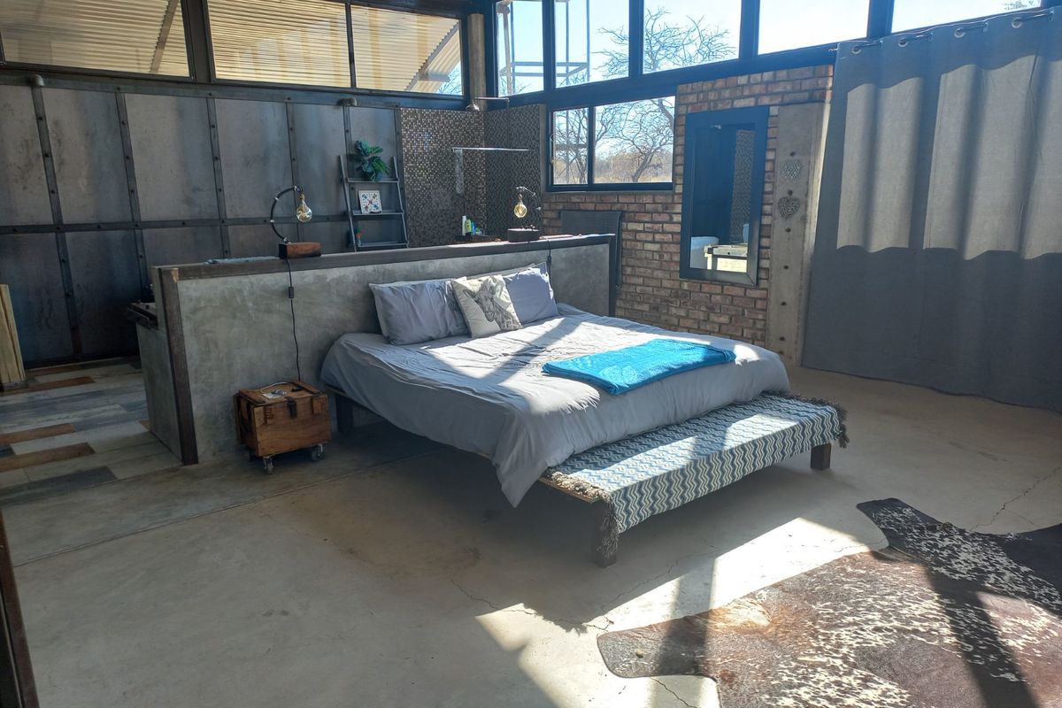 Spacious bedroom featuring industrial design elements, including exposed brickwork, a concrete partition wall, polished concrete flooring, and expansive windows with natural light.