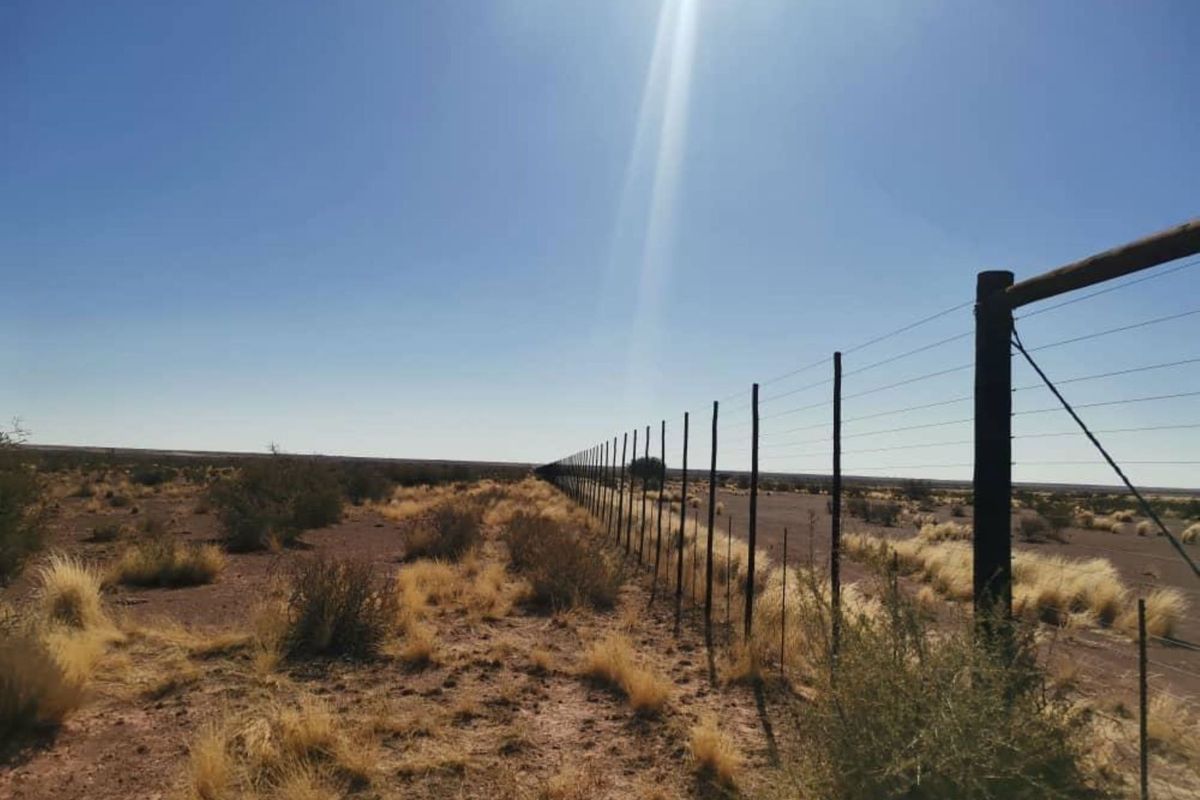 A view of the farm perimeter featuring a long wire fence line stretching across the arid landscape.