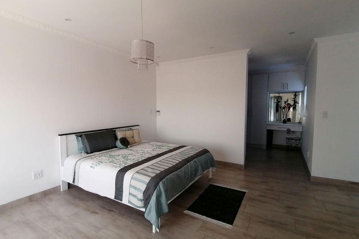 Spacious bedroom featuring wood-look tile flooring, recessed ceiling lighting, decorative crown molding, and an integrated dressing area with built-in cabinetry.
