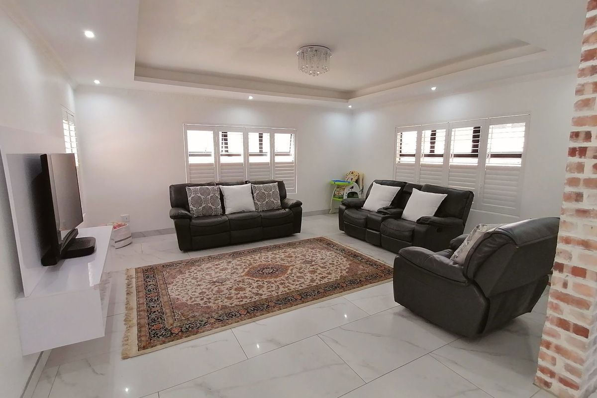 Spacious living room featuring polished marble-style floor tiles, recessed tray ceiling with downlights, and white plantation shutters on the windows.