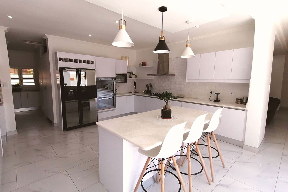 Modern open-plan kitchen featuring white cabinetry, stone countertops, a central island with breakfast bar seating, and integrated stainless steel appliances.