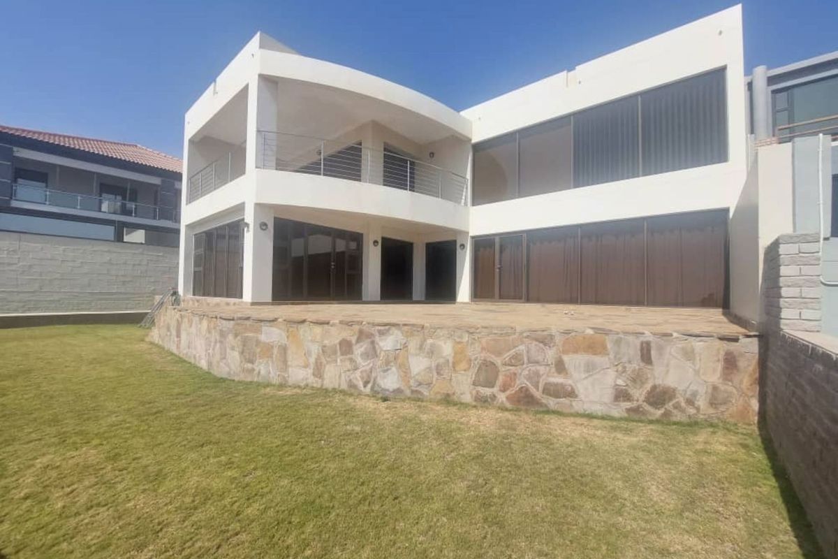 Rear view of a modern two-story house featuring a stone-clad retaining wall, expansive patio area, and large glass sliding doors opening to the garden.