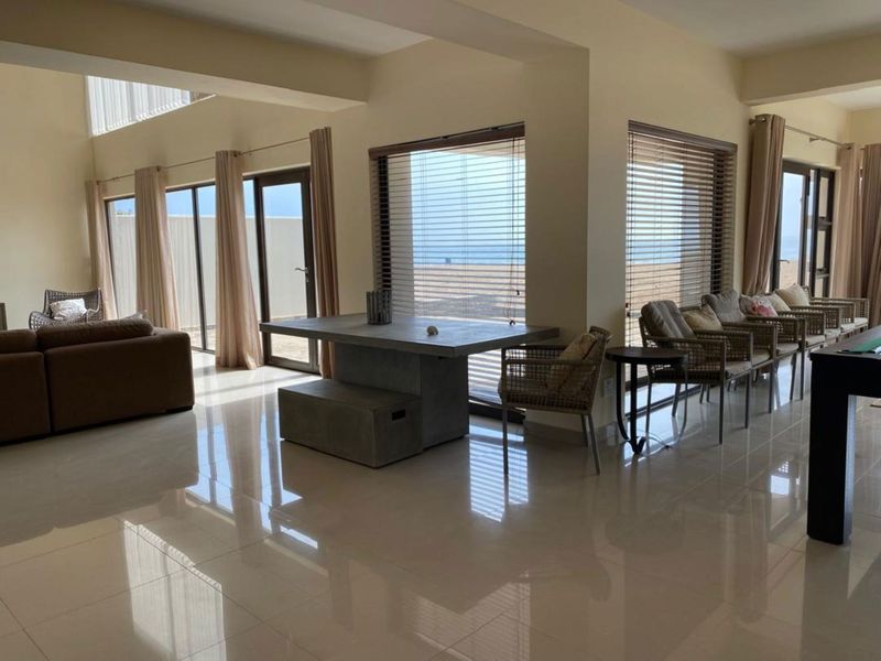 Spacious open-plan living and dining area featuring large windows with ocean views, tiled flooring, and direct access to the exterior.