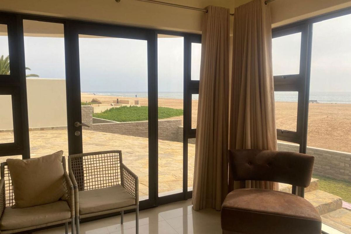 A bright living area featuring large floor-to-ceiling glass doors that open onto a patio with direct beach and ocean views.