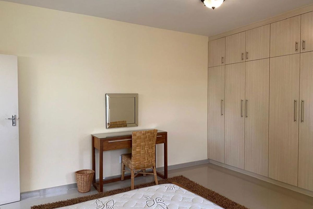 A well-maintained bedroom featuring extensive built-in floor-to-ceiling cabinetry with light wood-grain finish and neutral tiled flooring.