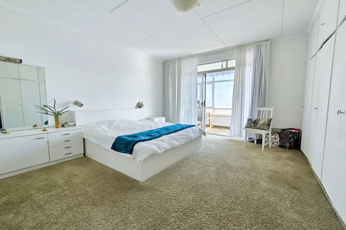 Spacious bedroom featuring built-in cupboards, neutral walls, and direct access to a private balcony through sliding glass doors.