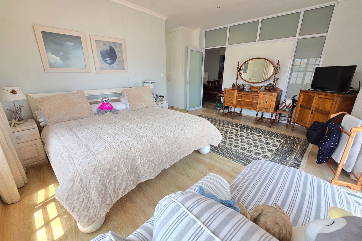 Spacious bedroom featuring light wood-look flooring, built-in cupboards, and a large glass-paneled partition wall leading to an adjacent living area.