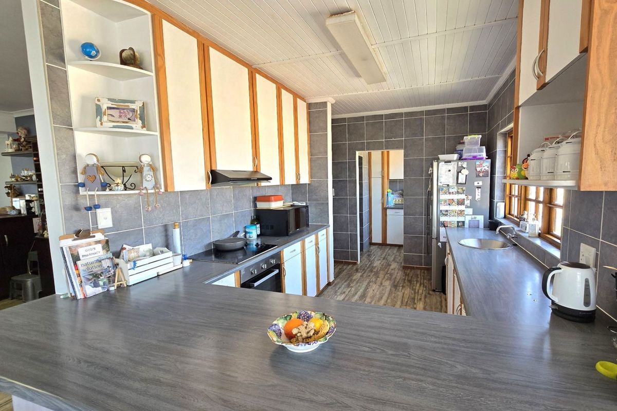 A functional kitchen featuring grey tiled walls, laminate countertops, built-in oven and hob, and ample cabinetry with an open-plan layout.
