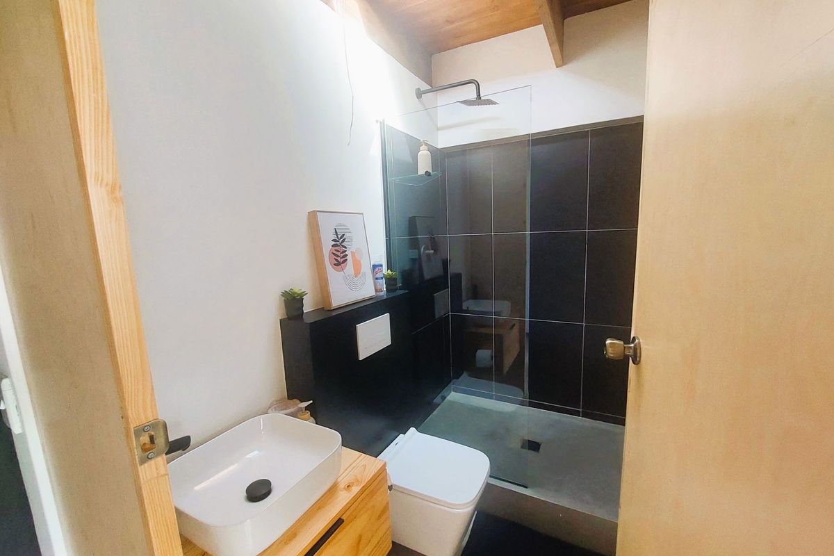 Modern bathroom featuring a walk-in shower with dark tiling, a wall-mounted toilet, and a contemporary vessel sink set on a wooden vanity.