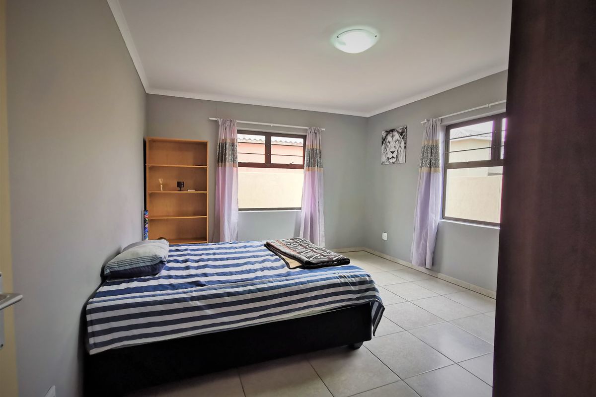 A well-lit bedroom featuring neutral wall tones, tiled flooring, and two windows providing natural light.