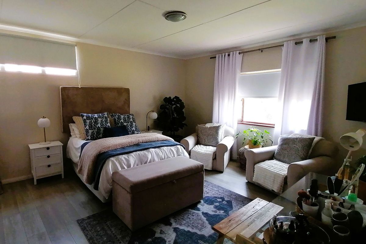 A spacious bedroom featuring light-toned laminate flooring, neutral wall finishes, and dual window treatments providing natural light.
