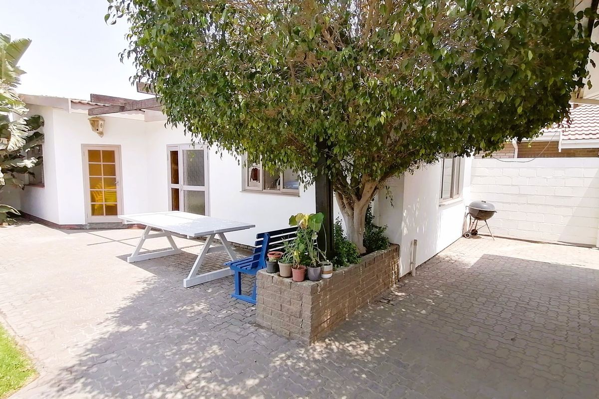 A paved rear courtyard area featuring a built-in brick planter box with a mature tree and direct access to the home.