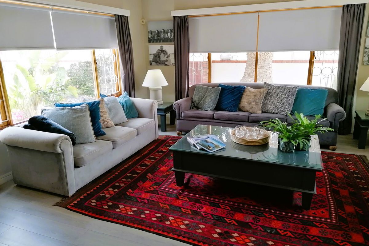 A comfortable living room featuring large windows with roller blinds, providing ample natural light and views of the garden.