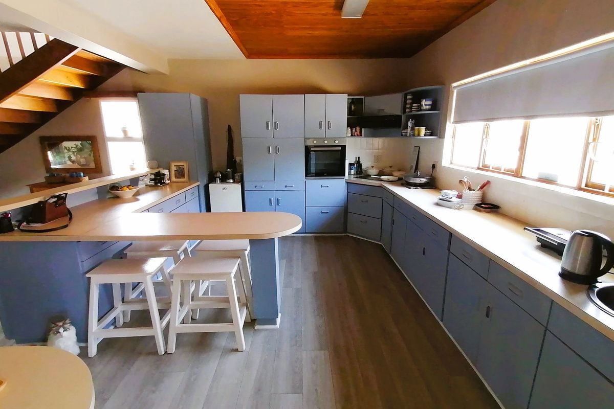 Spacious kitchen featuring blue cabinetry, integrated oven, laminate countertops, and a breakfast bar, set under a timber-paneled ceiling with adjacent staircase.