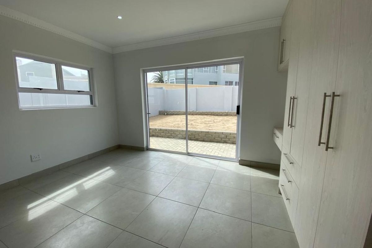 A bright bedroom featuring neutral floor tiles, built-in cabinetry, and sliding glass doors that open onto a paved rear courtyard area.