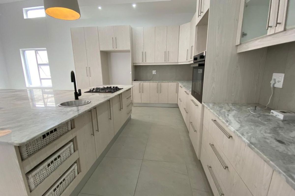 Modern kitchen featuring light wood cabinetry, stone countertops, a central island with a sink, and built-in oven and gas hob.