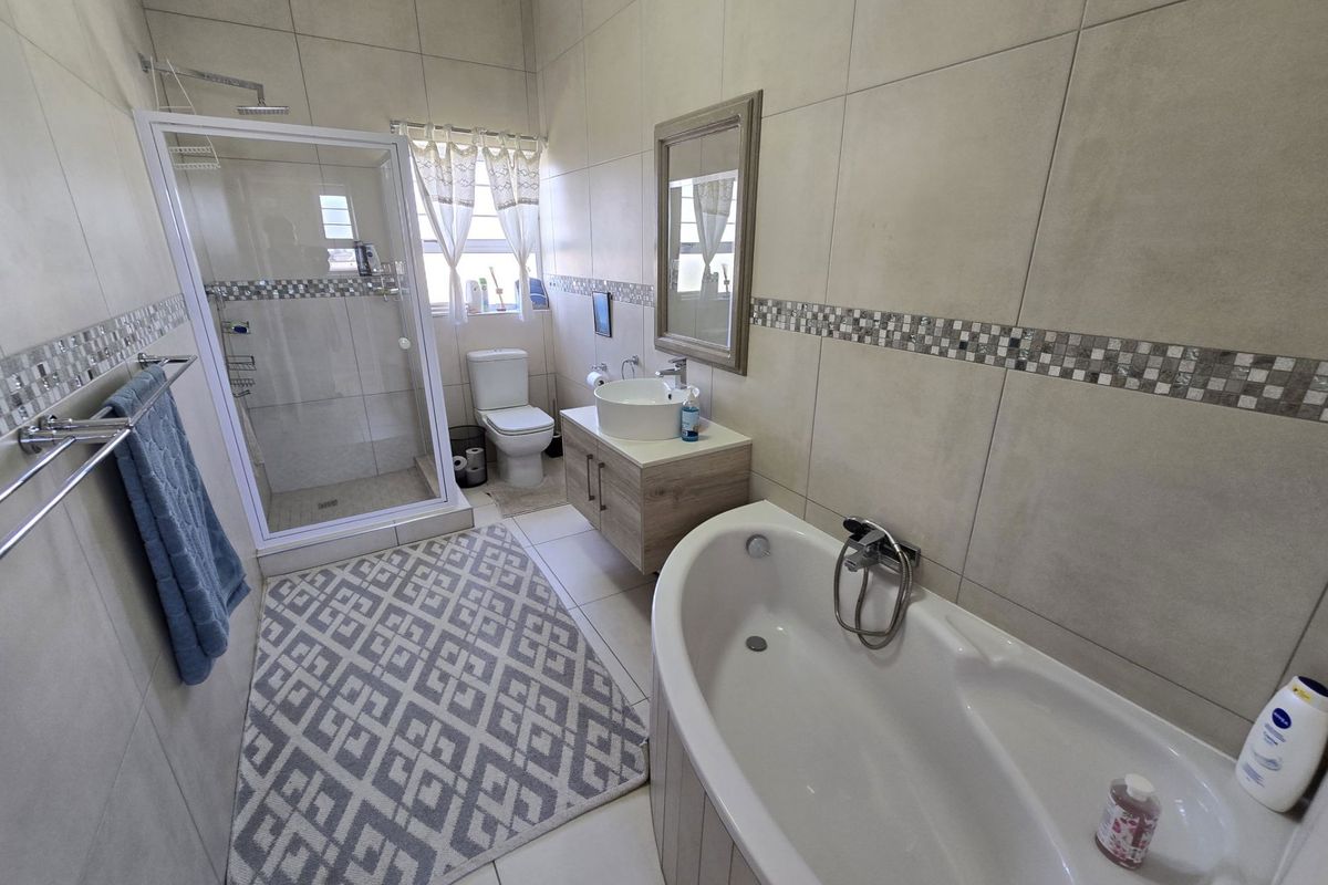 A well-maintained bathroom featuring a glass-enclosed shower, a modern vanity with a vessel sink, a bathtub, and neutral wall tiling with decorative mosaic accents.