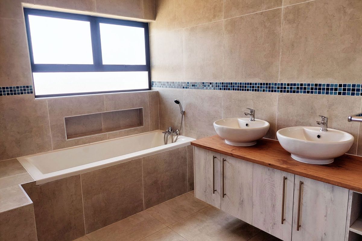 Modern bathroom featuring a built-in bathtub, dual vessel sinks on a wooden vanity, and neutral wall tiling with a decorative mosaic accent strip.