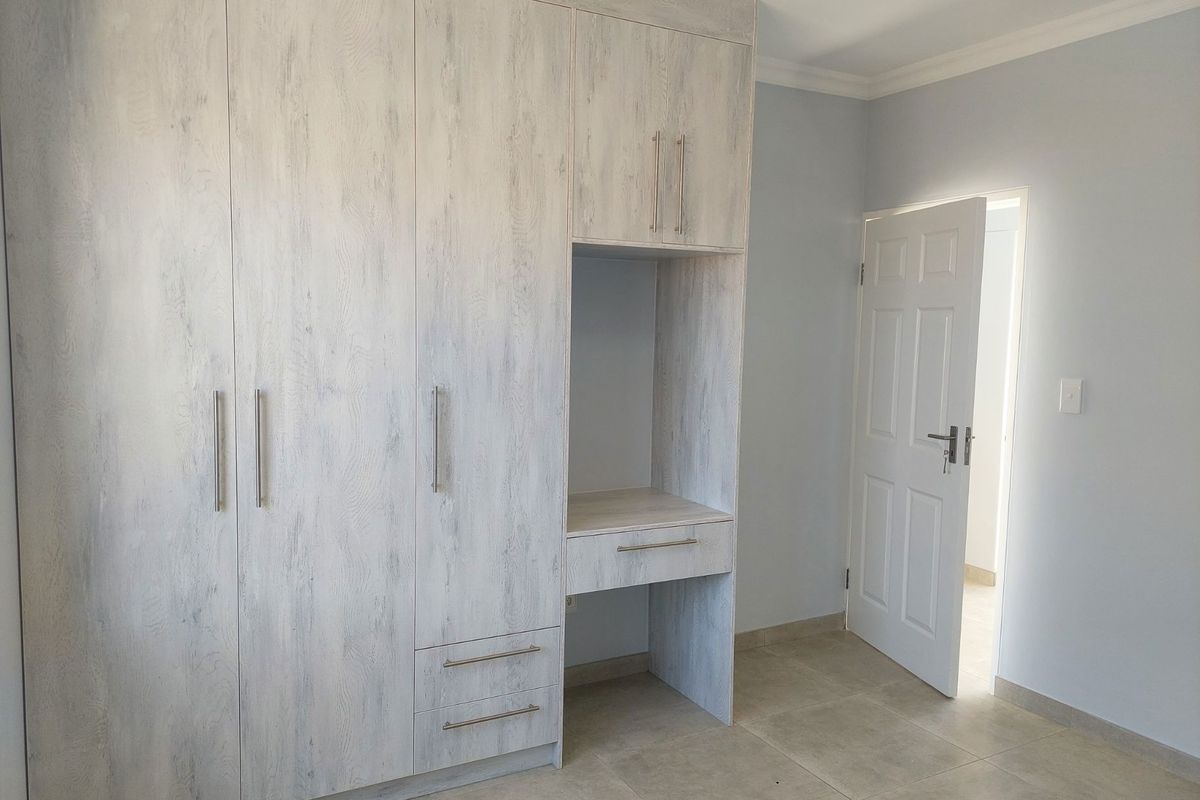 A bright bedroom featuring light wood-grain built-in cupboards with an integrated vanity desk and tiled flooring.