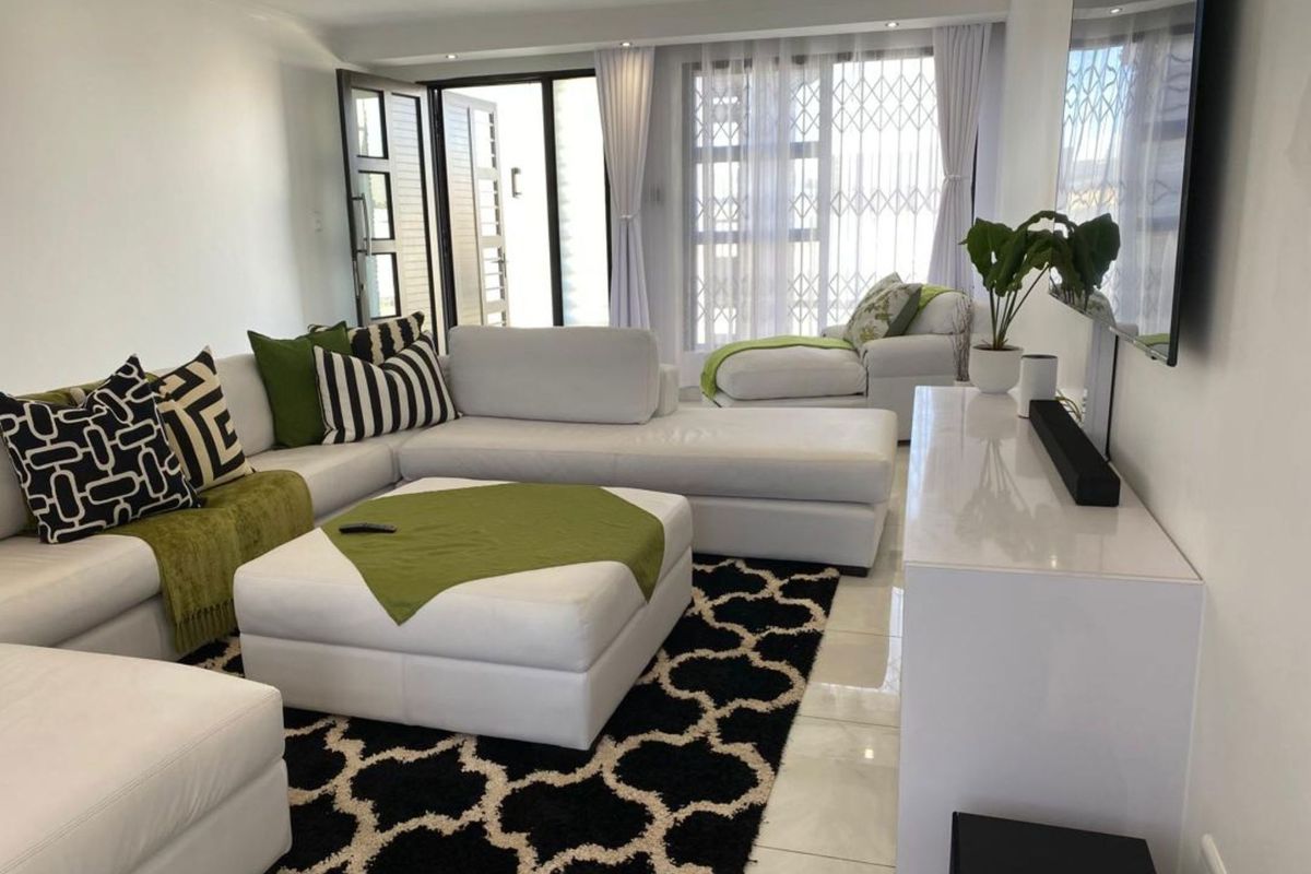A bright and modern living room featuring polished floor tiles, recessed ceiling lighting, and large glass doors leading to an outdoor area.