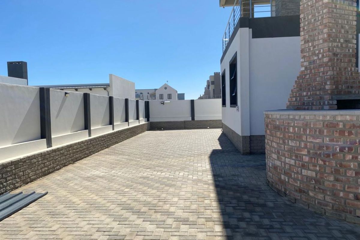A spacious paved rear courtyard featuring a built-in brick braai area, enclosed by high boundary walls and adjacent to the main dwelling structure.