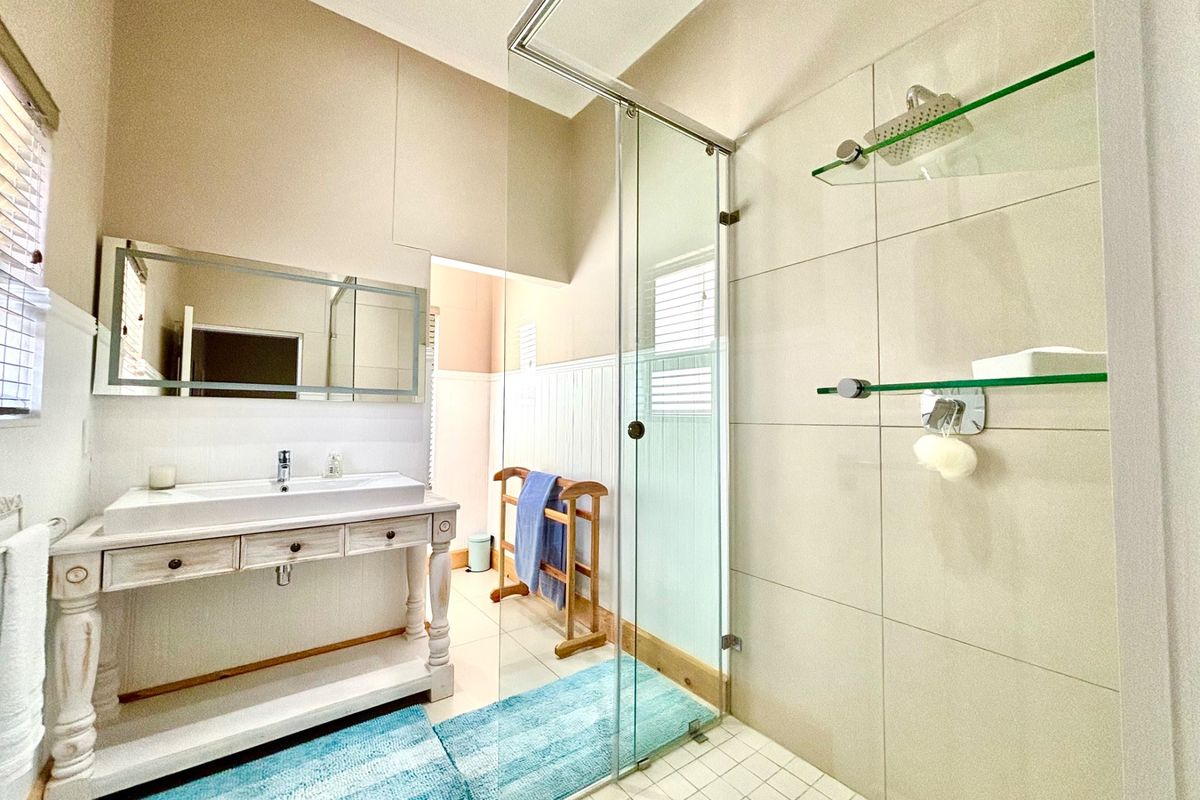A bright bathroom featuring a glass-enclosed shower, a vanity with a basin, and wall-mounted glass shelving.
