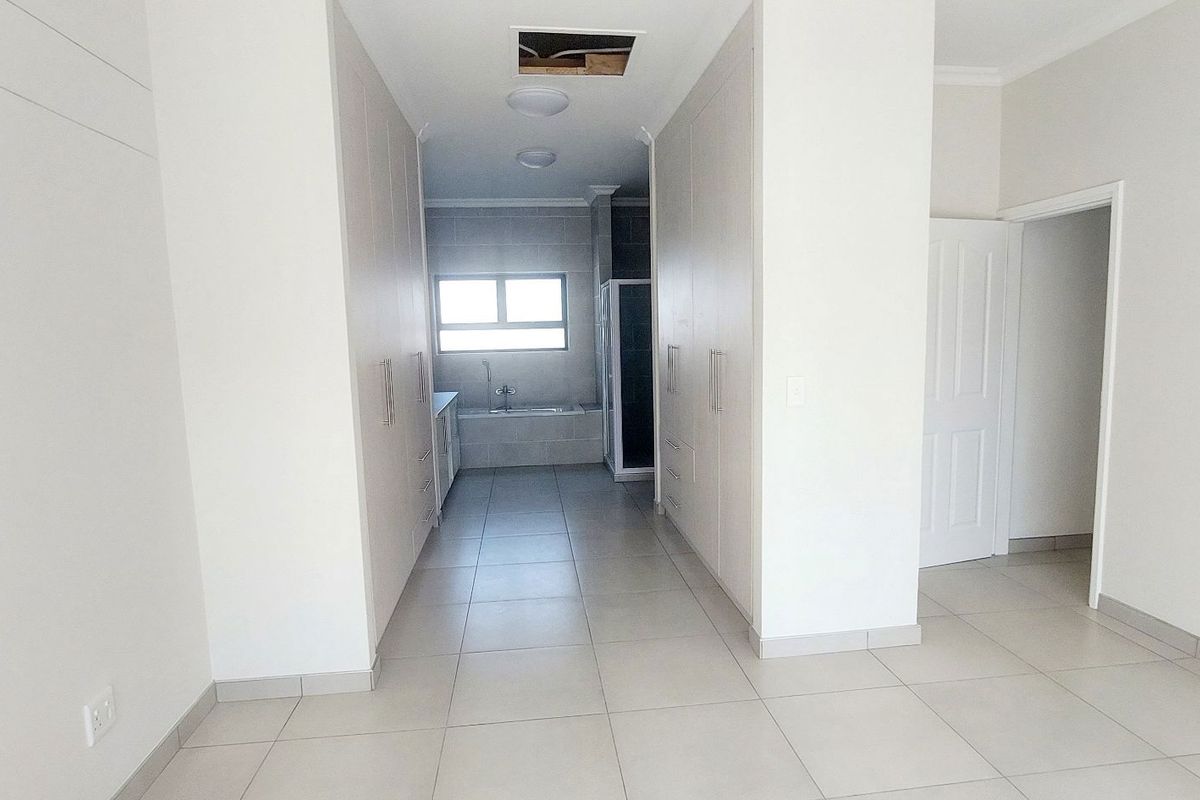 A spacious dressing area featuring extensive built-in cabinetry, leading directly into an en-suite bathroom with tiled flooring throughout.