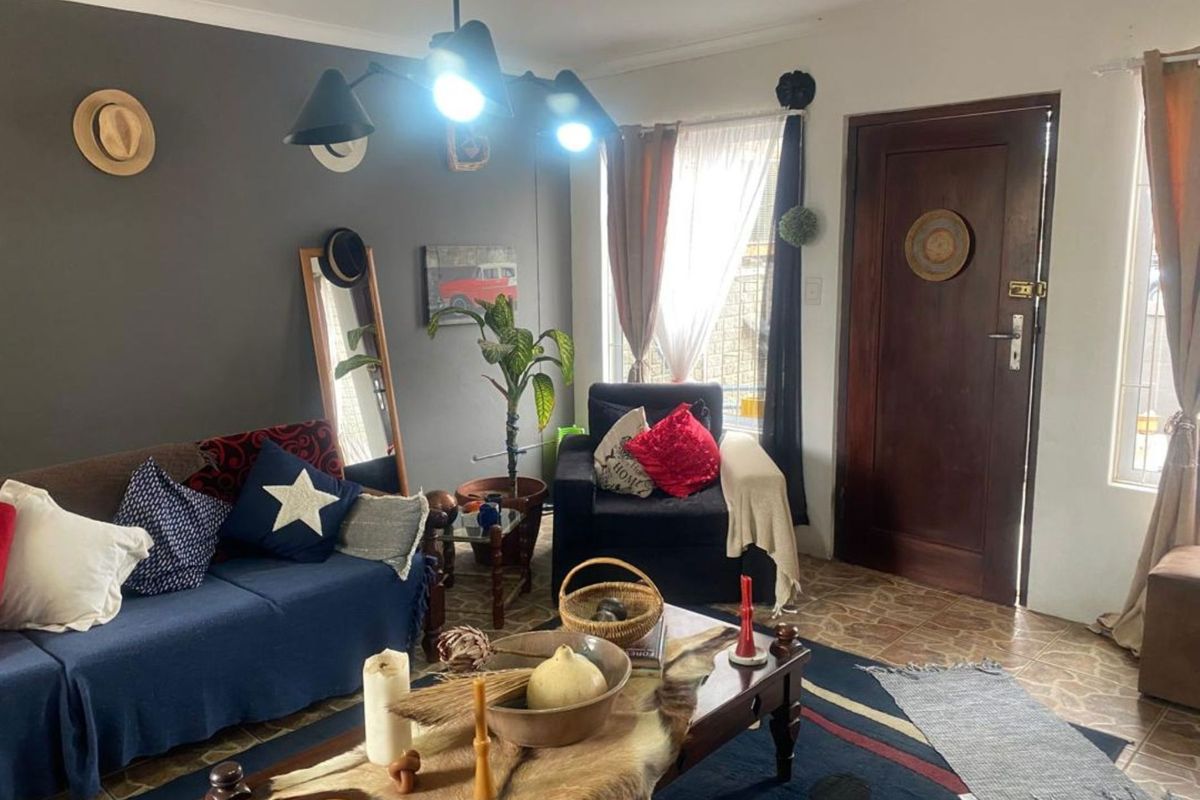 A living room featuring tiled flooring, a dark accent wall, and a wooden entrance door with security gate.
