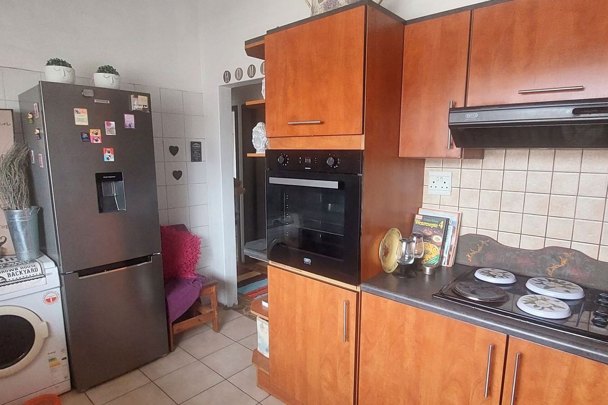 A functional kitchen featuring wooden cabinetry, a built-in oven, an extractor fan, and a tiled backsplash with integrated laundry appliance space.