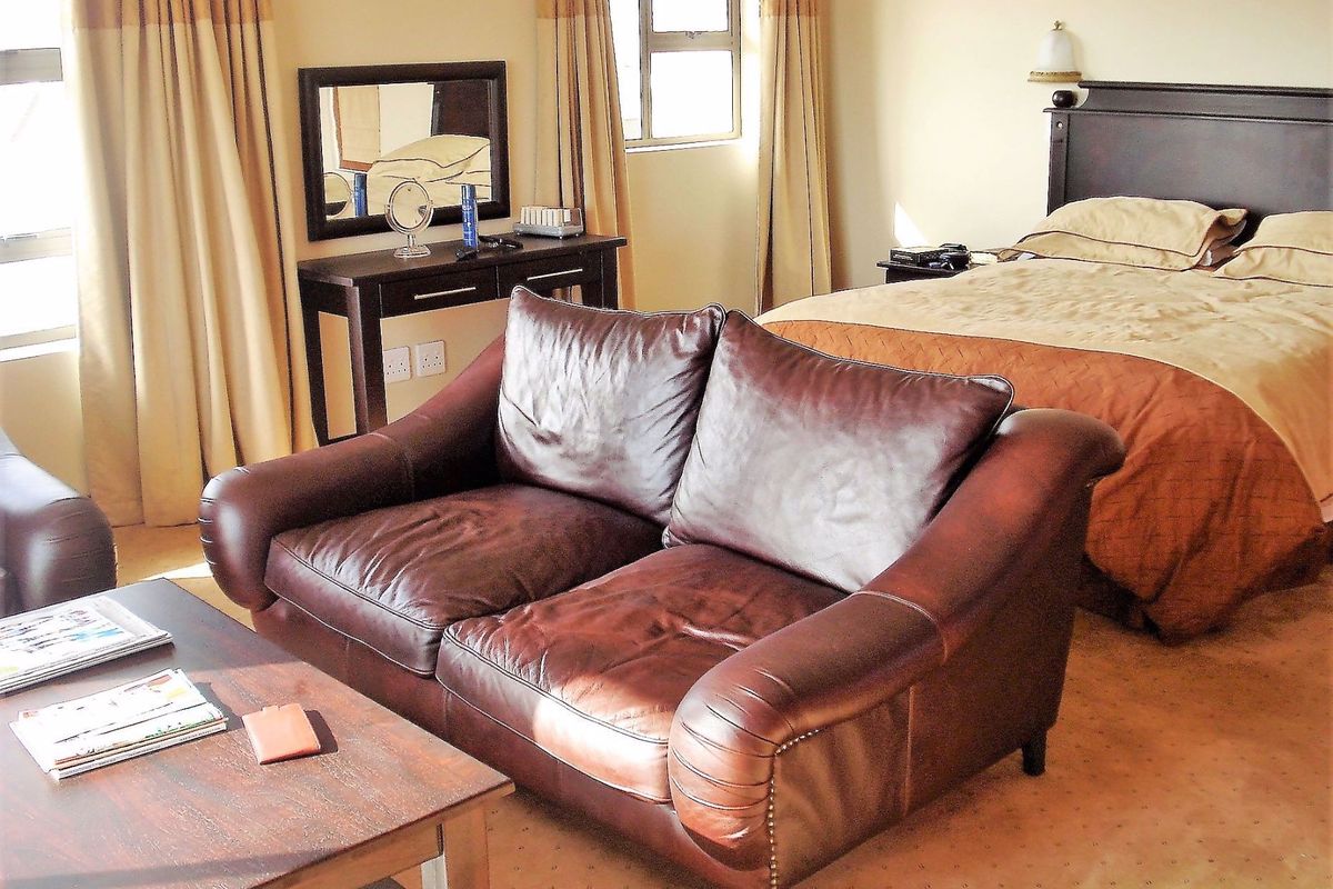 A spacious bedroom featuring neutral carpeting, large windows with curtains, and a dedicated seating area, offering a comfortable and functional living space.