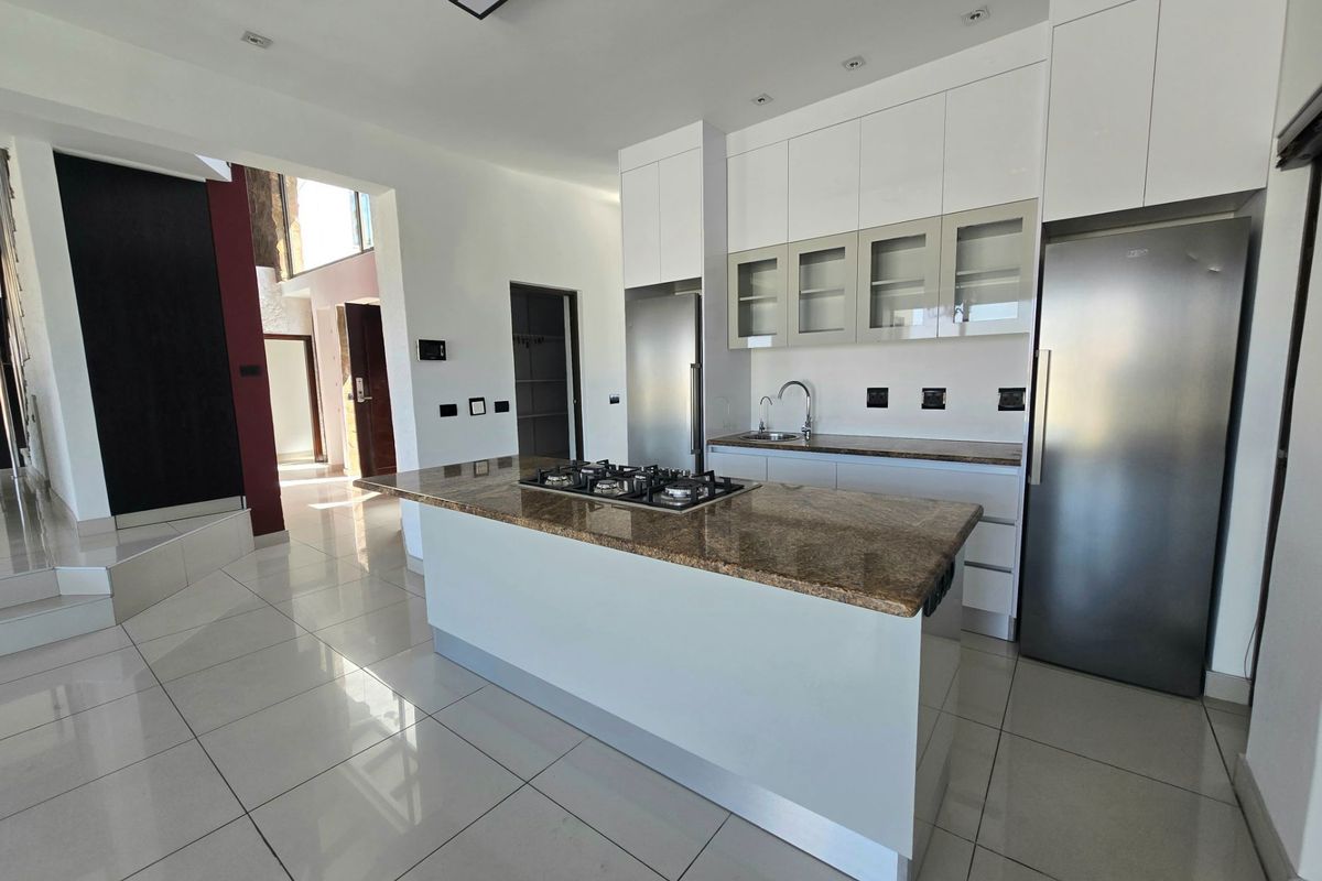 Modern kitchen featuring a central island with a built-in gas hob, granite countertops, high-gloss cabinetry, and tiled flooring throughout.