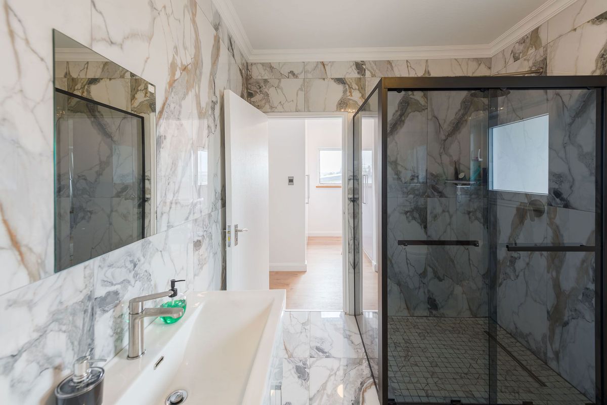 Modern bathroom featuring floor-to-ceiling marble-look tiling, a sleek glass-enclosed walk-in shower, and a contemporary wall-mounted vanity basin.