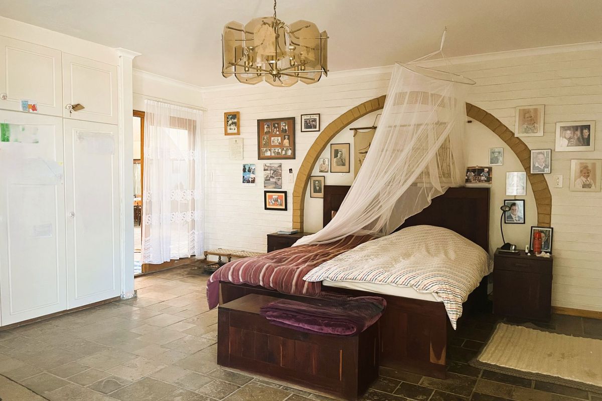 Spacious bedroom featuring stone tile flooring, built-in cupboards, and a decorative brick arch detail, offering a rustic farm-style aesthetic.
