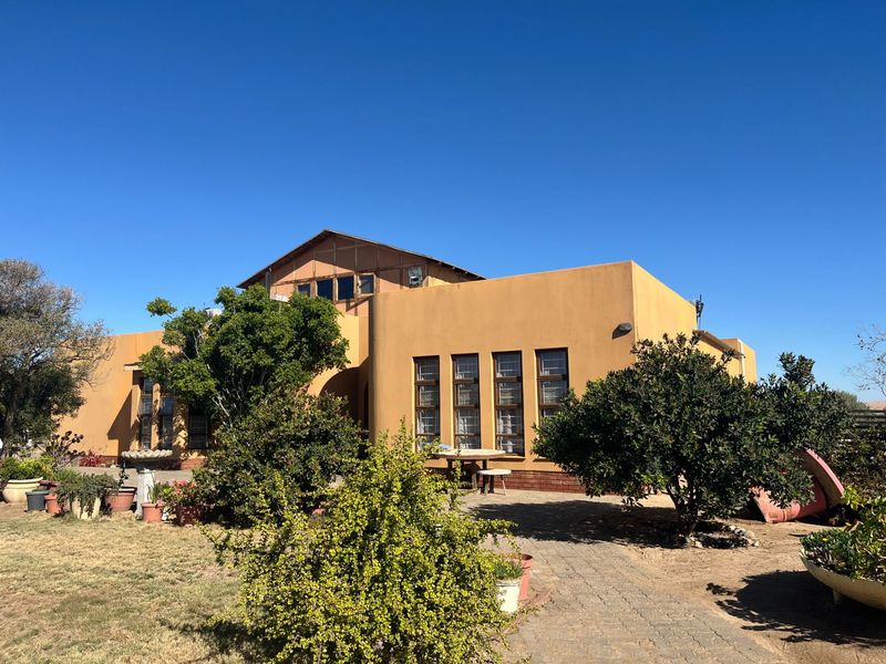 Rear view of a farm-style residence featuring a stucco facade, multi-pane windows, and a paved walkway leading through the garden area.