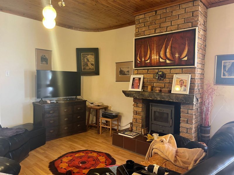 Cozy living room featuring a prominent brick fireplace with a wood-burning stove, timber ceiling, and laminate flooring.