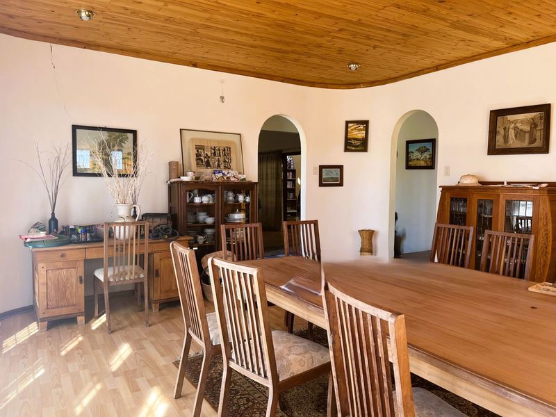 A dining room featuring timber ceiling paneling, laminate flooring, and arched doorways leading to adjacent living spaces.