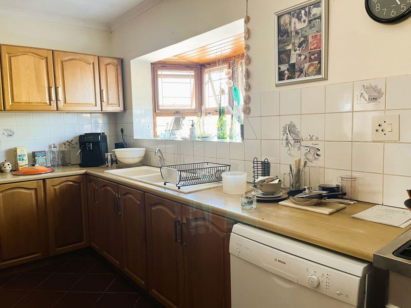 A functional kitchen featuring traditional wooden cabinetry, laminate countertops, a double basin sink, and a bright bay window with tiled backsplash.