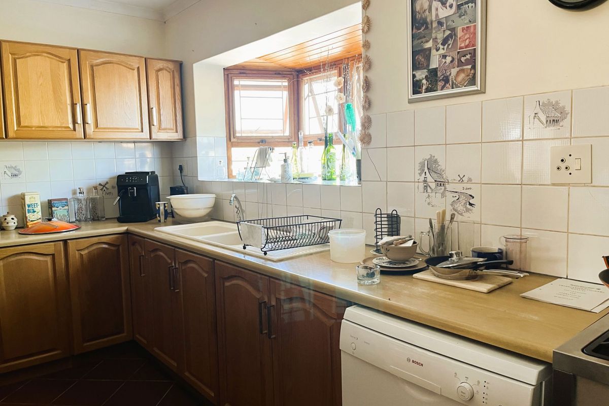A functional kitchen featuring traditional wooden cabinetry, laminate countertops, a double basin sink, and a bright bay window with tiled backsplash.