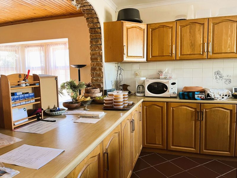 A functional kitchen featuring traditional wooden cabinetry, laminate countertops, a tiled backsplash, and a distinctive brick archway leading to the adjacent living area.