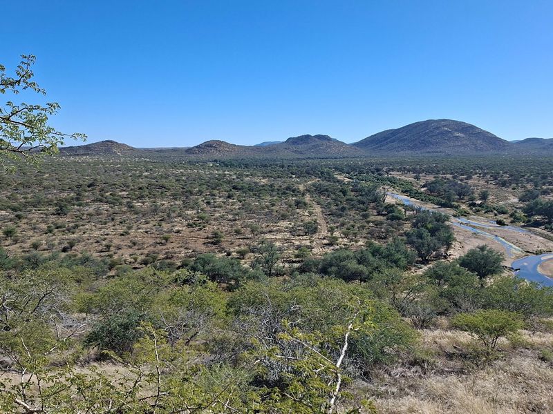 A scenic elevated view of the expansive farm landscape featuring natural vegetation, rolling hills, and a winding riverbed.