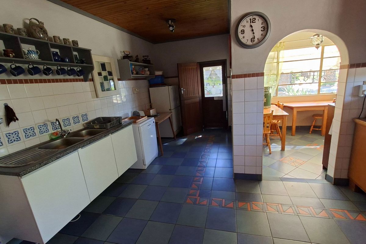 A functional kitchen featuring tiled flooring, a double sink, built-in cabinetry, and an arched transition leading to an adjacent dining area.
