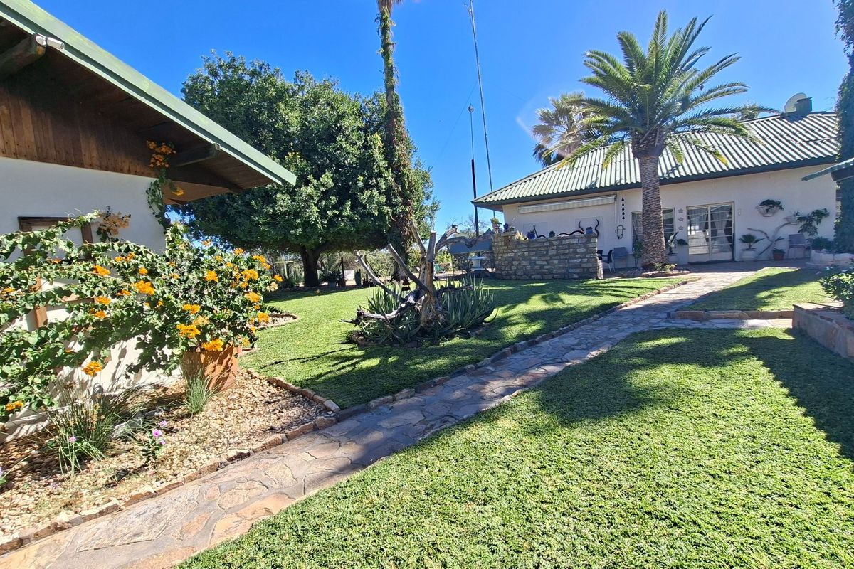 A well-maintained rear garden area featuring a stone paved walkway, lush lawn, and established landscaping between the farm building structures.