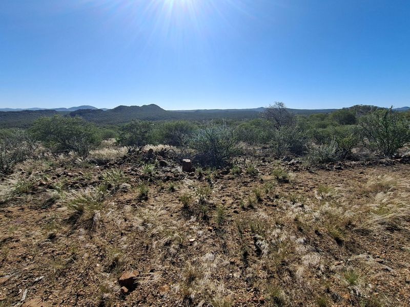 A wide-angle view of the natural farm landscape featuring rolling hills and indigenous vegetation under a clear blue sky.