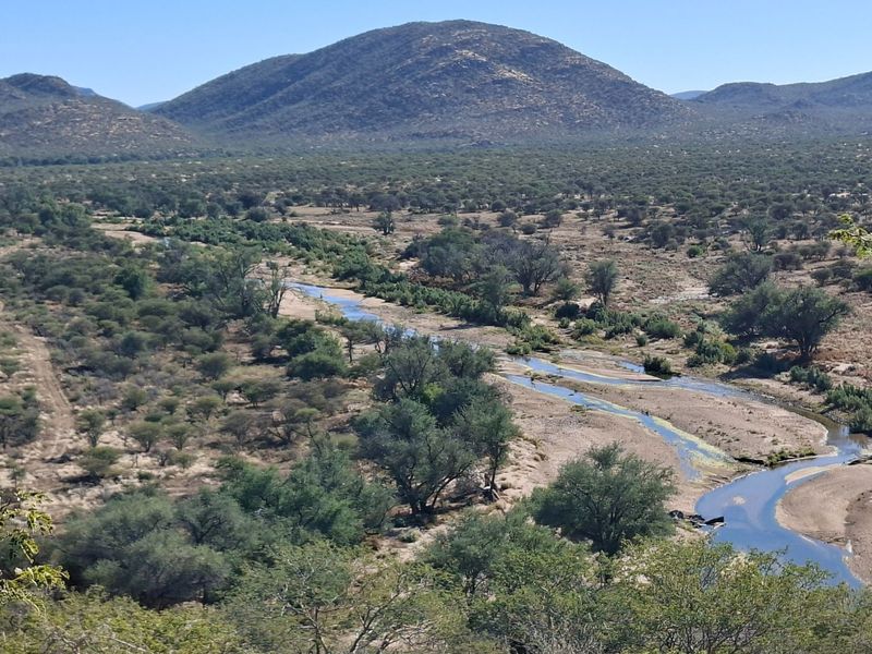 Expansive scenic view of the farm landscape featuring natural vegetation, rolling hills, and a winding riverbed.