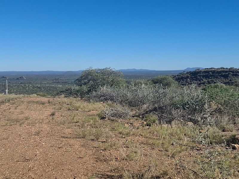 Expansive landscape view overlooking the farm terrain with natural vegetation and distant hills under a clear blue sky.