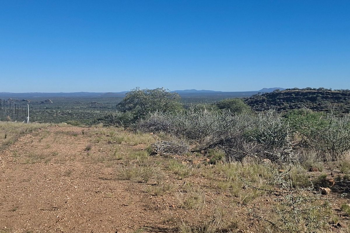 Expansive landscape view overlooking the farm terrain with natural vegetation and distant hills under a clear blue sky.