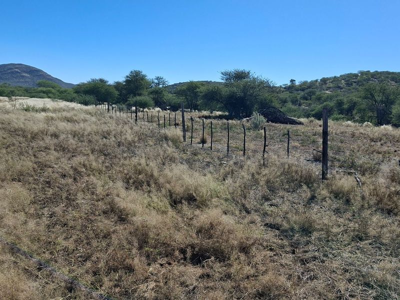 A wide-angle view of the farm landscape featuring natural vegetation, a dirt track, and existing wire fencing.