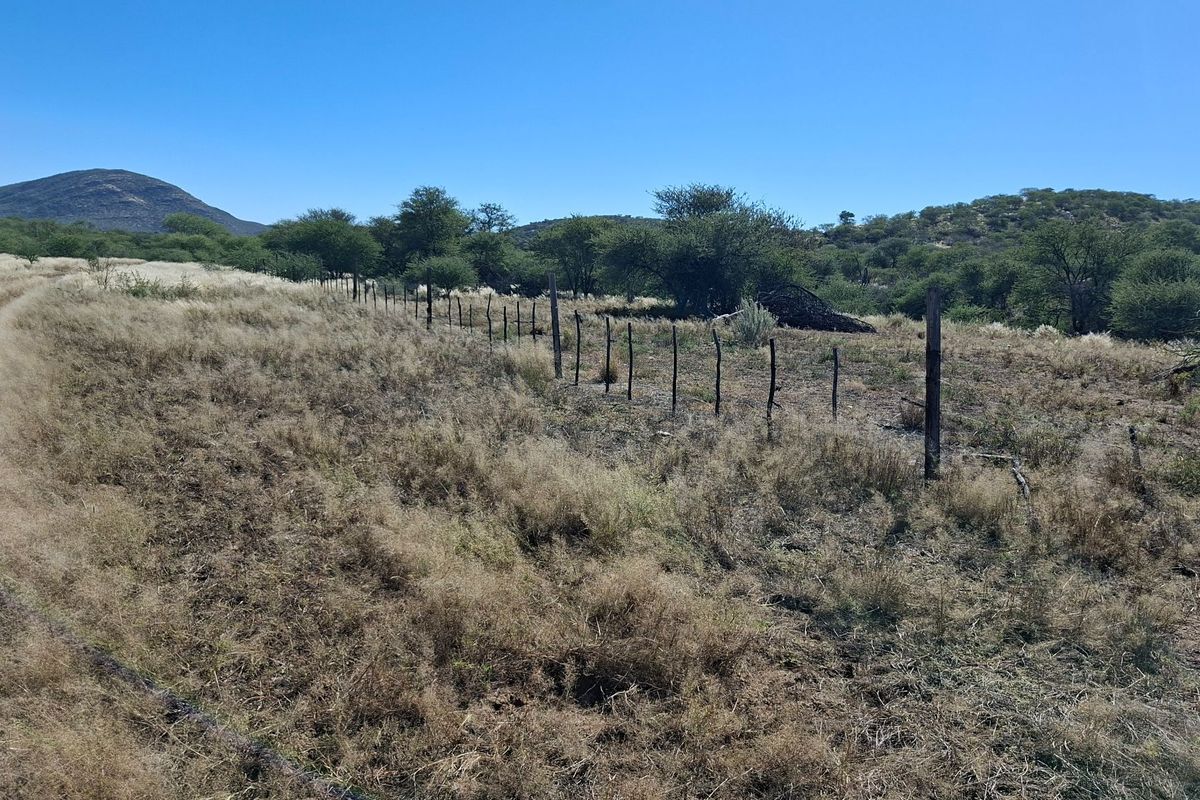 A wide-angle view of the farm landscape featuring natural vegetation, a dirt track, and existing wire fencing.